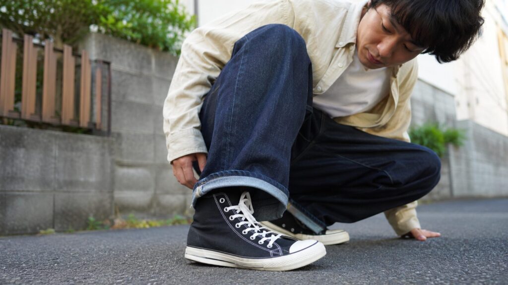 日本人男性が屋外でしゃがみ、黒いハイカットスニーカーのつま先横に曲げ負荷がかかっている様子